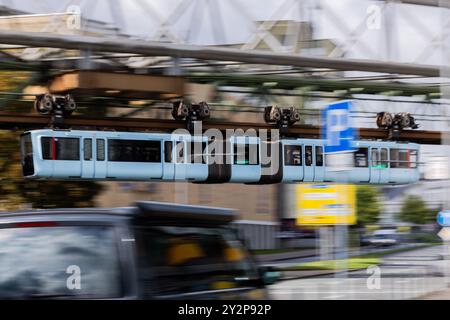 Wuppertal, Deutschland. September 2024. Eine Schwebebahn führt über eine Straße. Laut Marco Polo Trendguide`25 entwickelt sich die Stadt im Bergischen Land derzeit zu einer Art Kunsthochburg: „Wenn man in Wuppertal unterwegs ist, glaubt man seinen Augen nicht. Hyper-realistische, poetische, surreale und abstrakte Wandmalereien prangen meterhoch an den Fassaden.“ Sie sind Teil des Projekts Urbaner Kunstraum Wuppertal (UKW), das bis Ende 2025 mit 24 großformatigen Gemälden Farbe in die Stadtteile bringen wird. Quelle: Rolf Vennenbernd/dpa/Alamy Live News Stockfoto